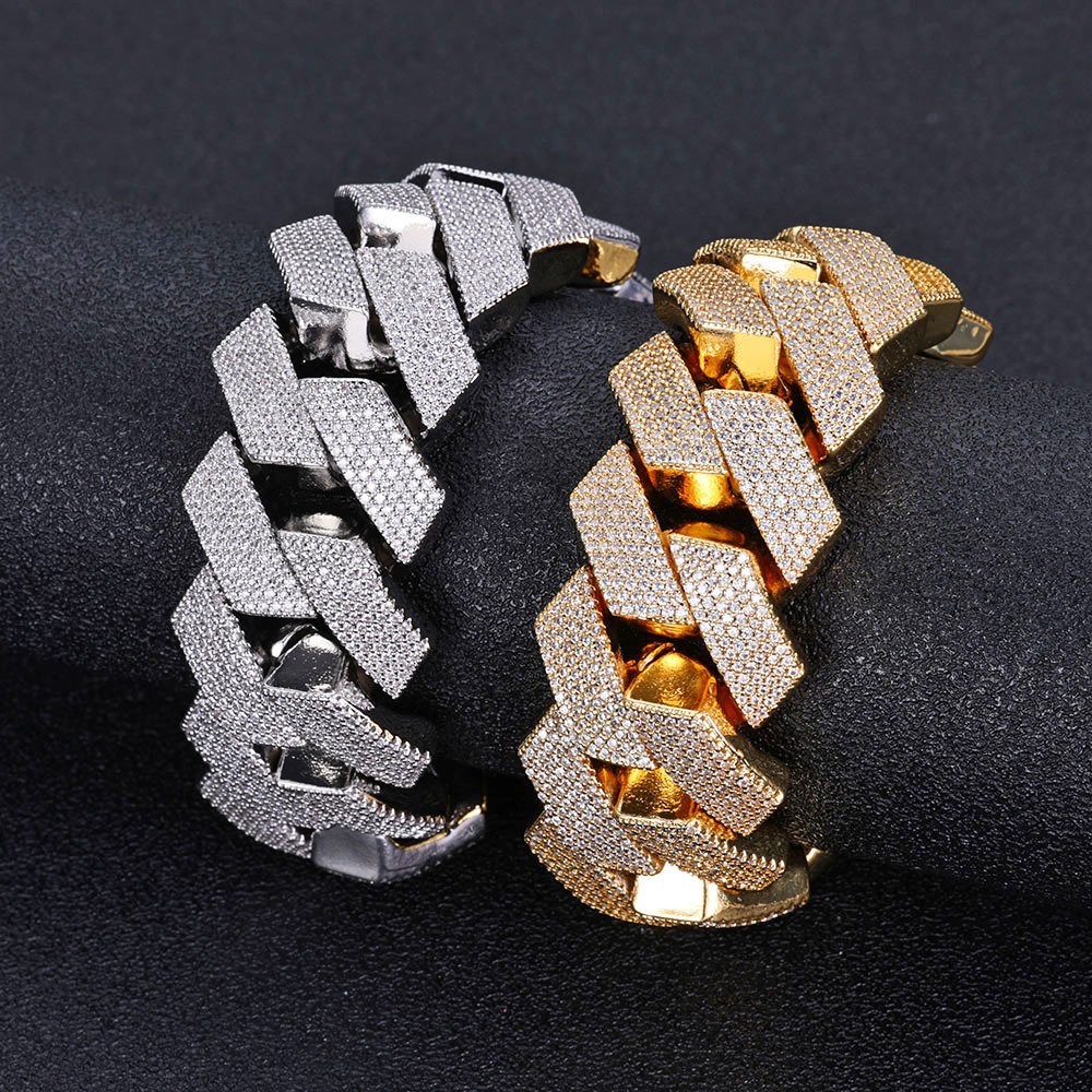 One silver and one gold 26mm oversized Cuban chain bracelet displayed on a round cylinder, simulating wrist wear.