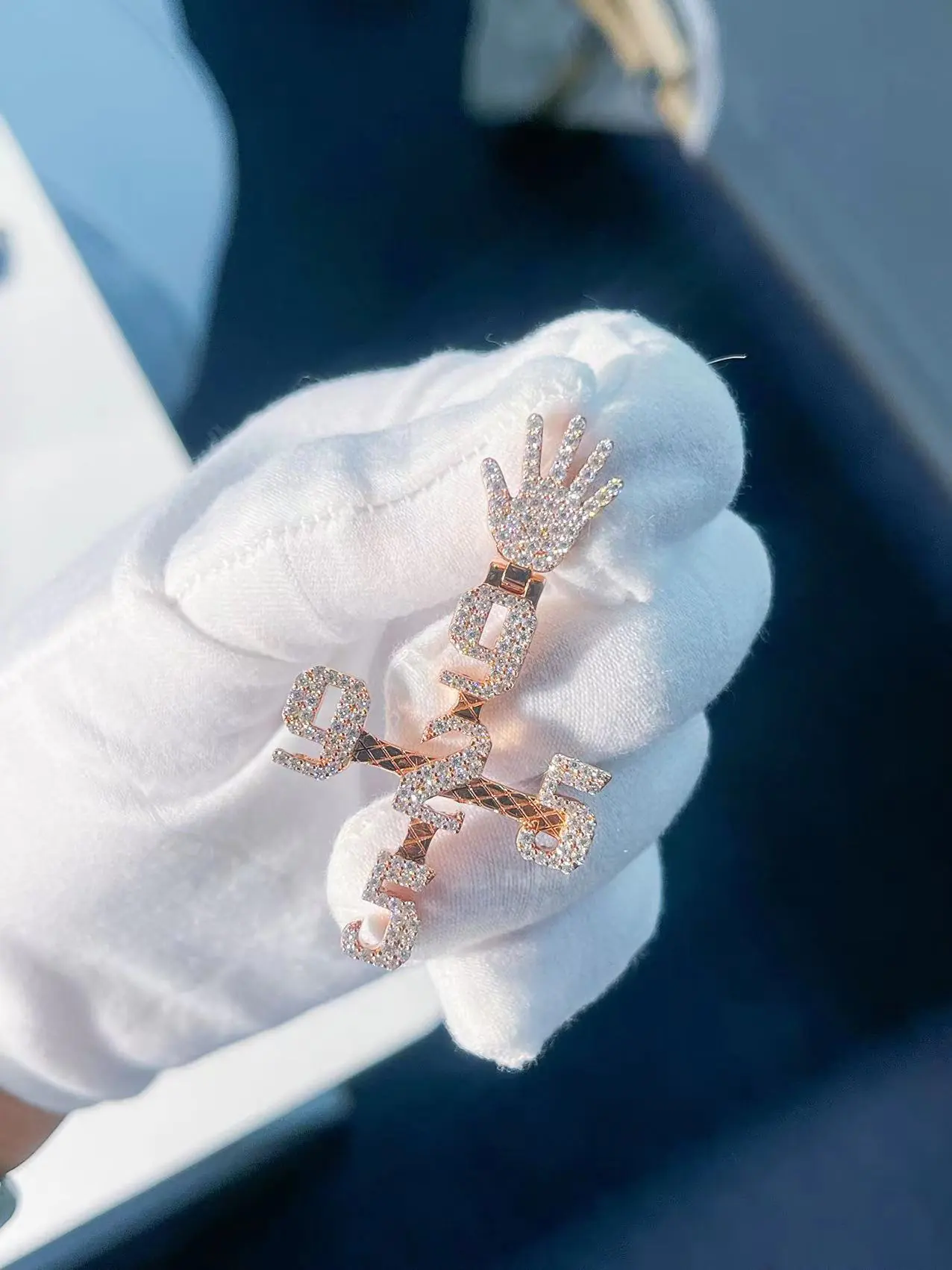 Iced out custom diamond numbers pendant with cross design and high-polish finish, held between fingers