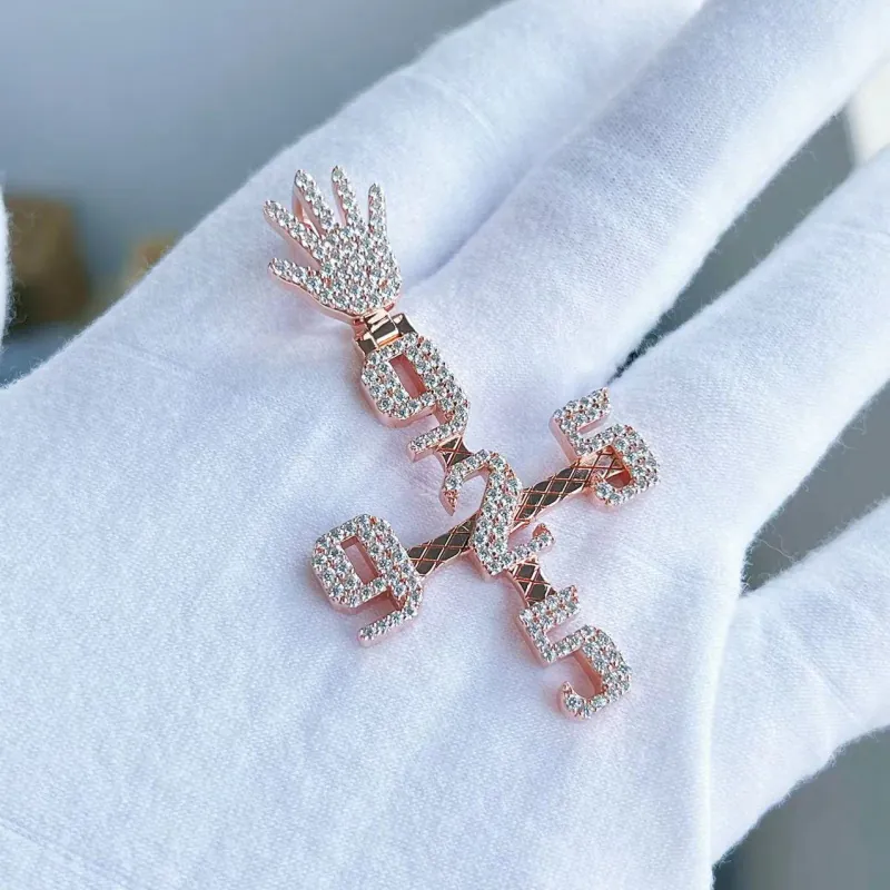Custom cross pendant in 925 silver with VVS moissanite, plated in 14K rose gold. Center features number 2, vertical and horizontal arms with “925”, bail shaped like a small hand, displayed on palm.