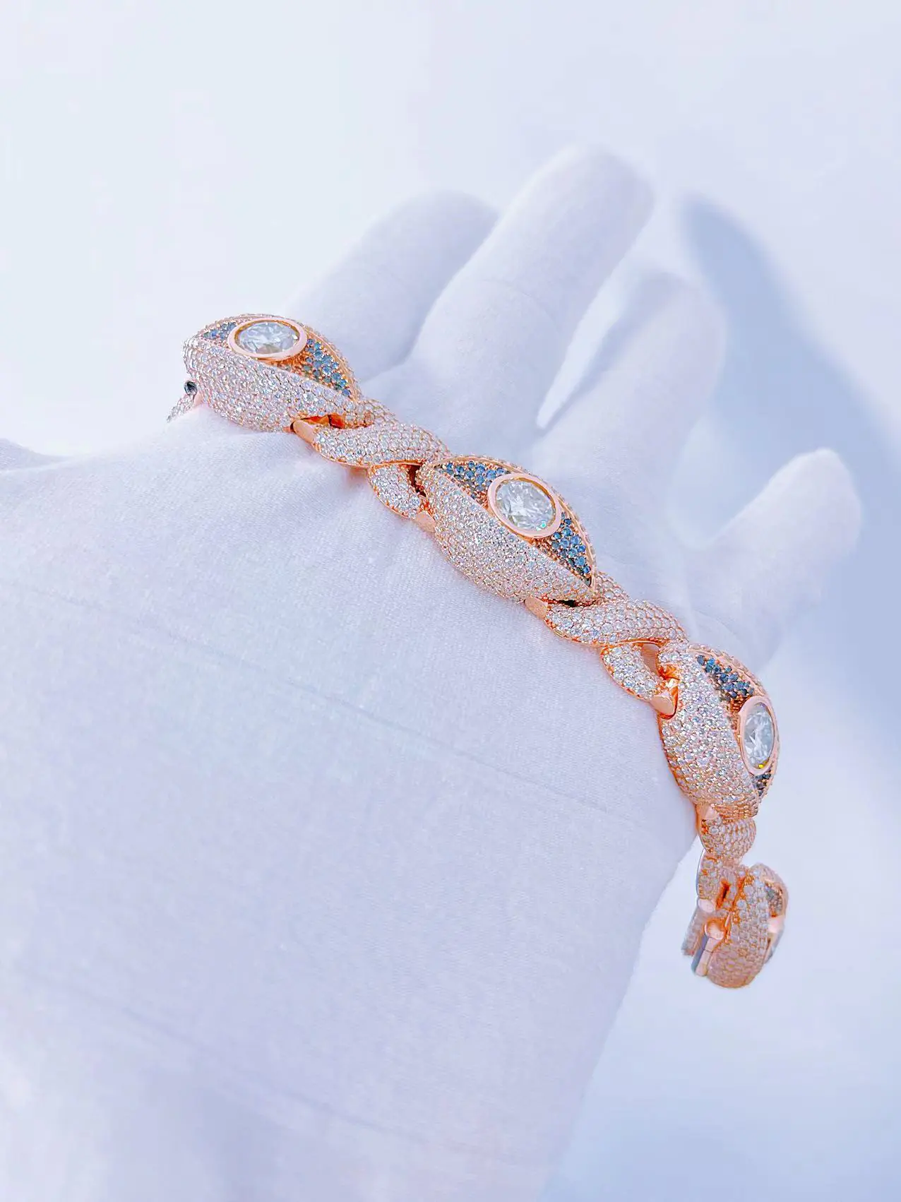 Side view of Infinity Eyes Cuban Chain bracelet in sterling silver with VVS moissanite, rose gold plated, 8mm wide, featuring blue and 0.5ct white stones