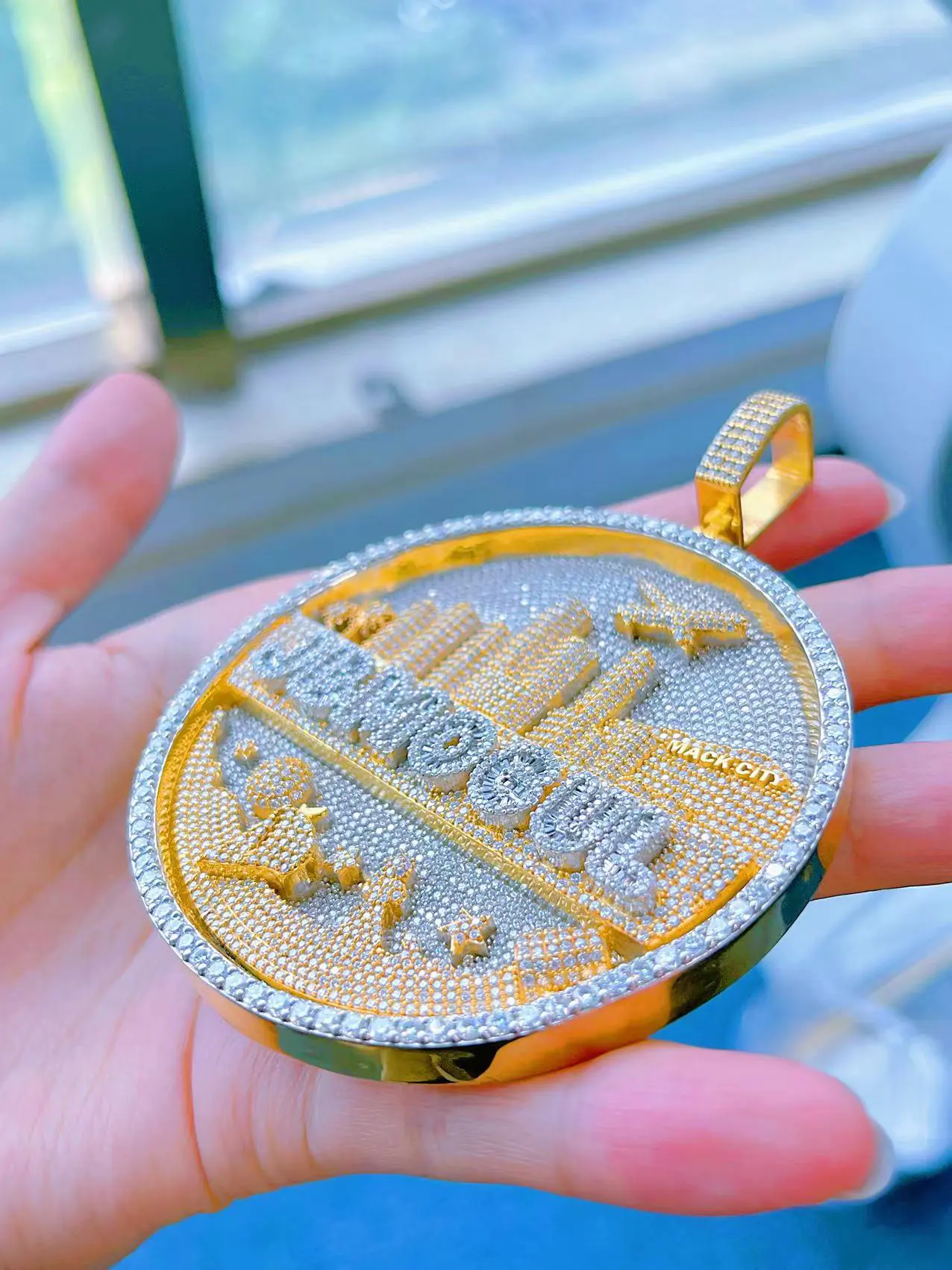 Left side view in hand of custom round skyline pendant in 925 silver with VVS moissanite, gold-plated skyline and white gold-plated background, fully iced.