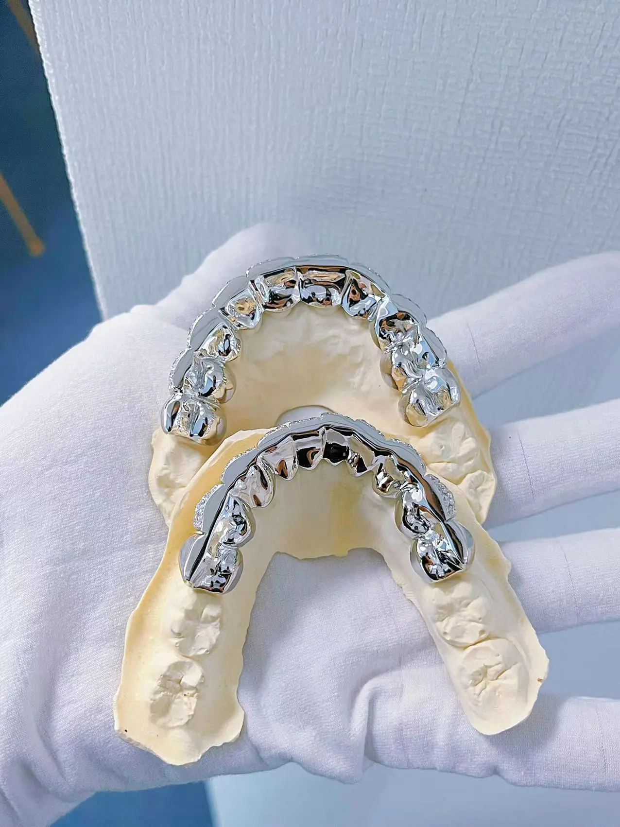 Top-down view in hand of custom fully iced grillz in 925 silver with VVS moissanite, 14K white gold plating, fully set with round-cut stones.