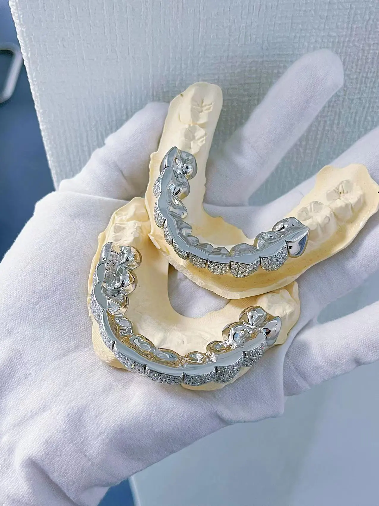 Top-down view in hand of custom fully iced grillz in 925 silver with VVS moissanite, 14K white gold plating, fully set with round-cut stones.