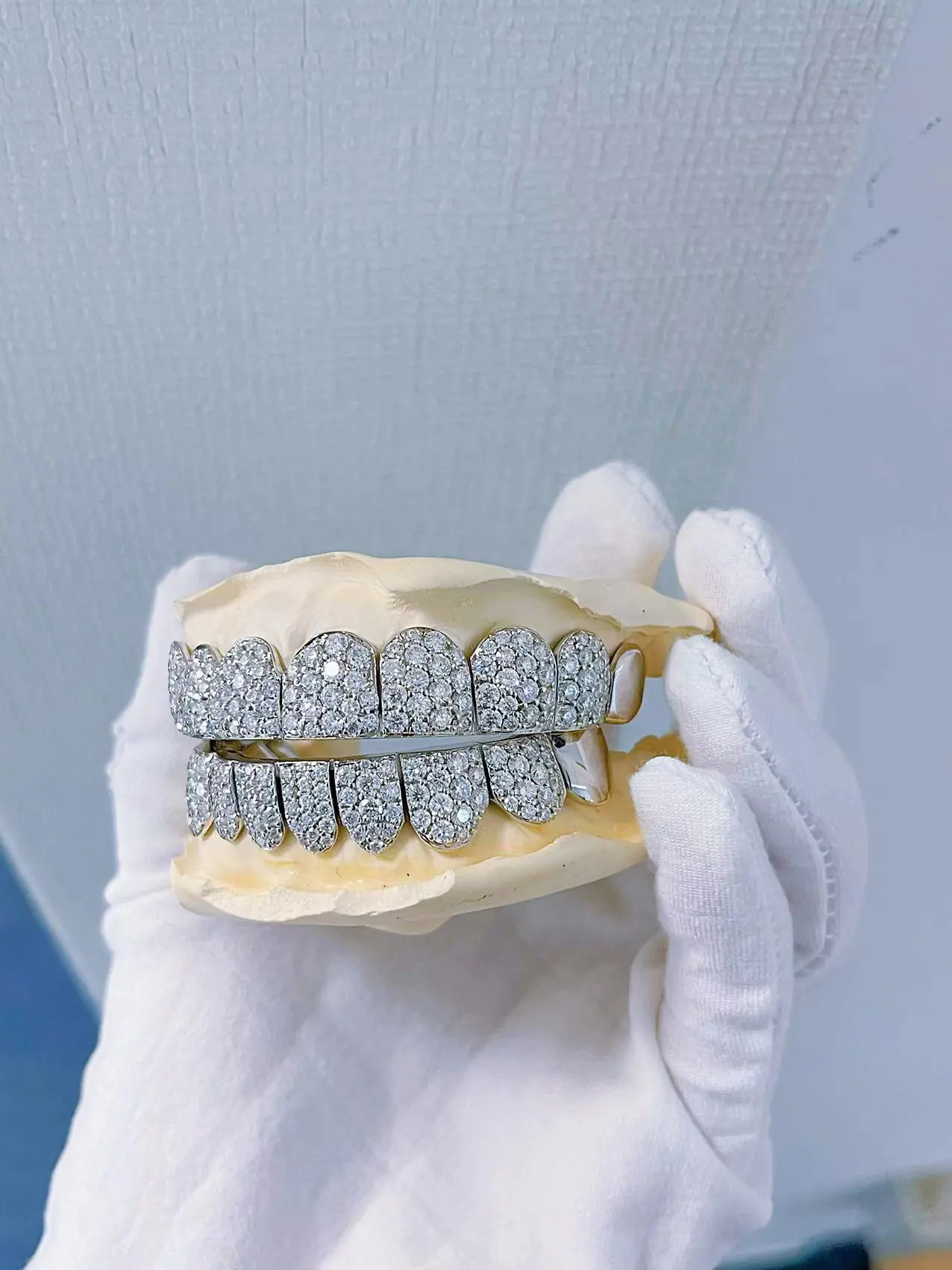 Close-up front detail view in hand of custom fully iced grillz in 925 silver with VVS moissanite, 14K white gold plating, round-cut stones.
