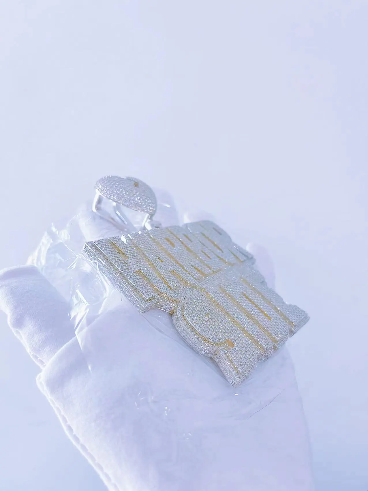 Left angled view of custom large letter name pendant in 925 silver with VVS moissanite, plated in 18K white gold, held in hand.