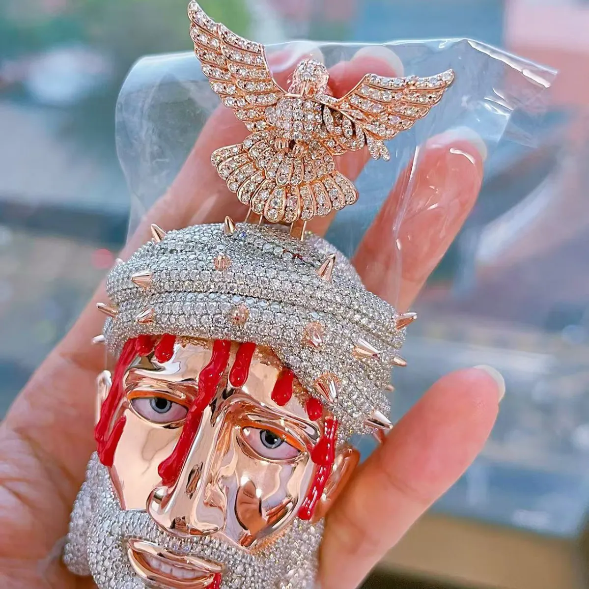 Close-up hand-held view of custom large Jesus pendant in 925 silver with VVS moissanite, showing 14K rose gold plated face, 14K white gold crown of thorns and beard, and red enamel blood accents.