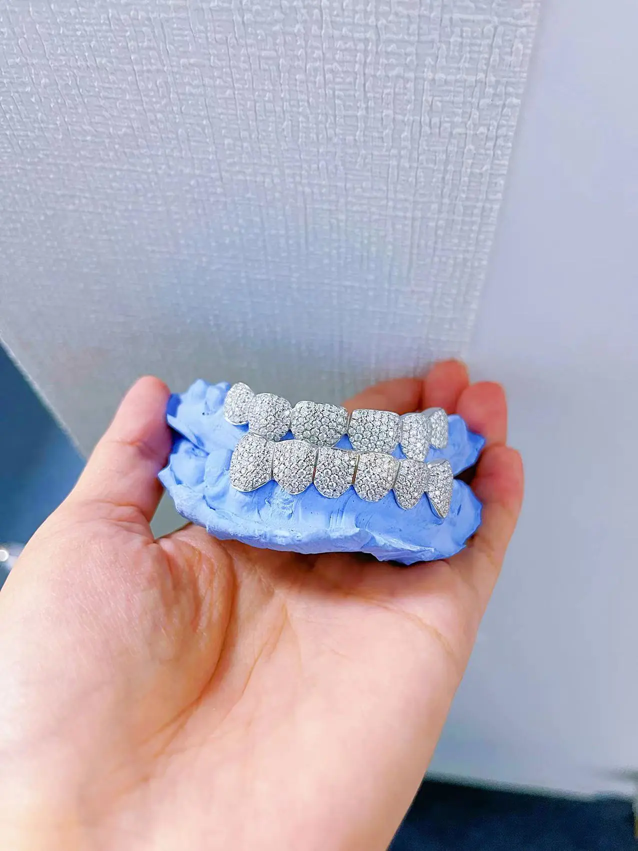 Close-up front detail view in hand of custom fully iced grillz in 925 silver with VVS moissanite, 14K white gold plating, round-cut stones.