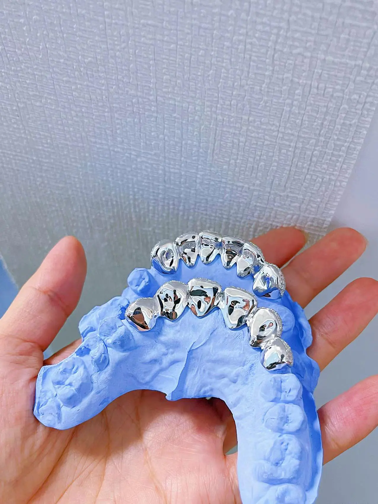 Top-down view in hand of custom fully iced grillz in 925 silver with VVS moissanite, 14K white gold plating, fully set with round-cut stones.