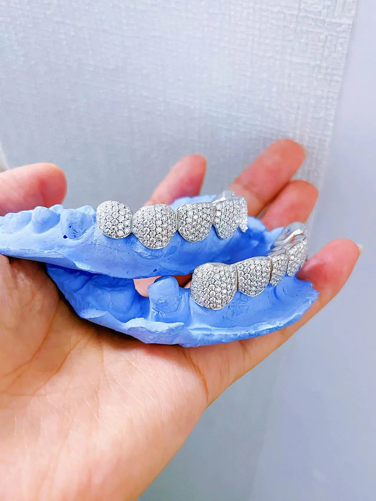 Hand-held side view of custom fully iced grillz in 925 silver with VVS moissanite, 14K white gold plating, showing round-cut stone details.