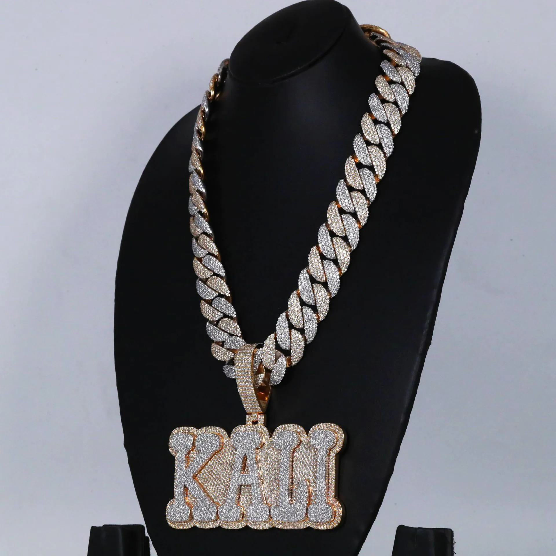 Left side view of custom large letter pendant in 925 silver with VVS moissanite, two-tone gold and white gold plating, hanging on 18mm fully iced Cuban link chain, worn on mannequin.