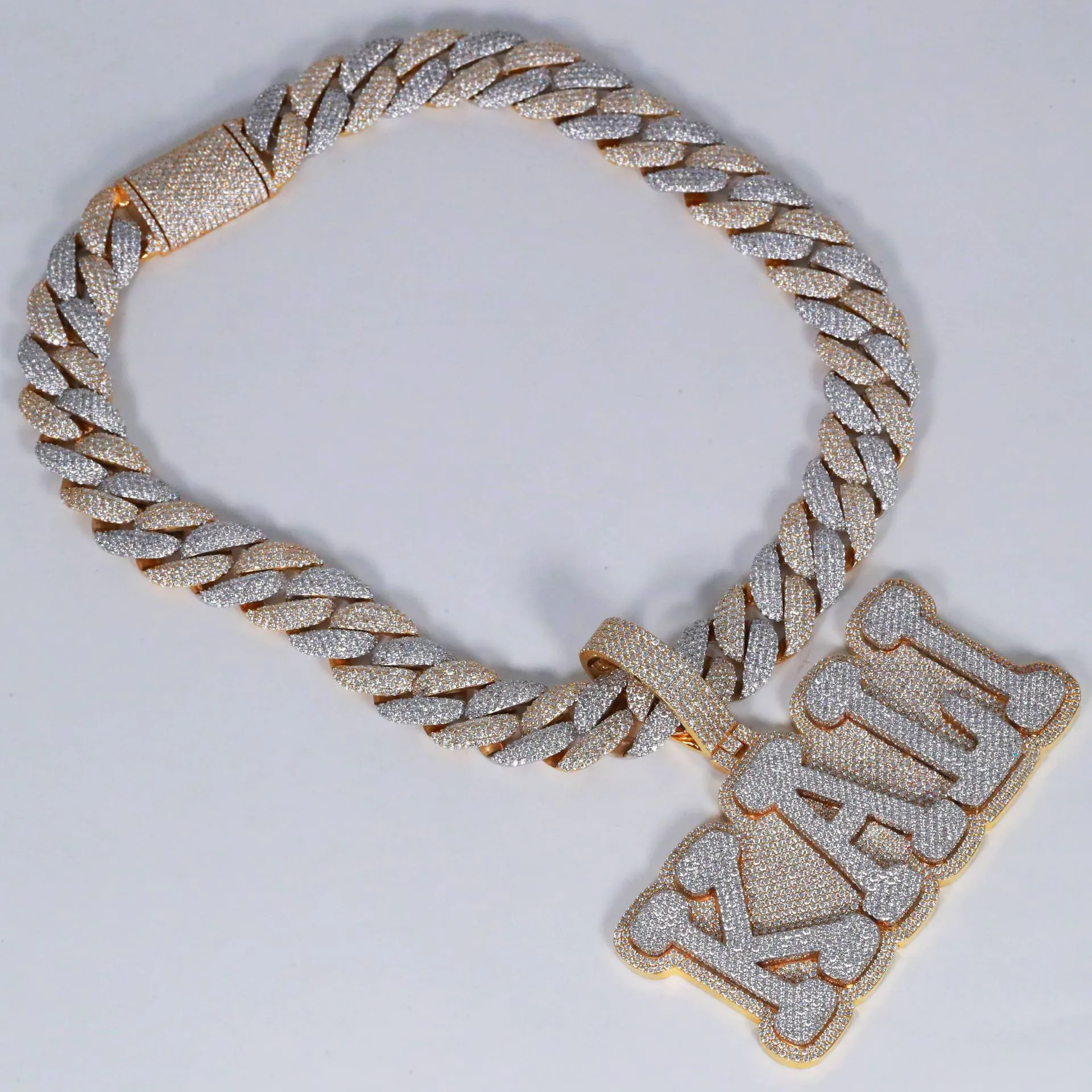 Custom large letter pendant in 925 silver with VVS moissanite, two-tone gold and white gold plating, attached to thick fully iced Cuban link chain, laid flat on table.