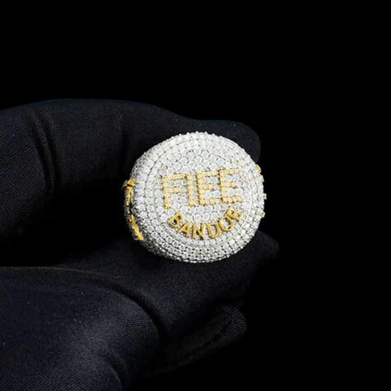 Close up of FIEE BANDOE Ring in sterling silver with moissanite, white gold plated, iced out ring held in hand, circular top showing FIEE letters with round white stones and BANDOE letters