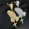 Two VVS Praying Hands Pendants in brass with CZ stones,   14K gold and 14K white gold plated,   held side by side in hand,   iced out hip hop jewelry