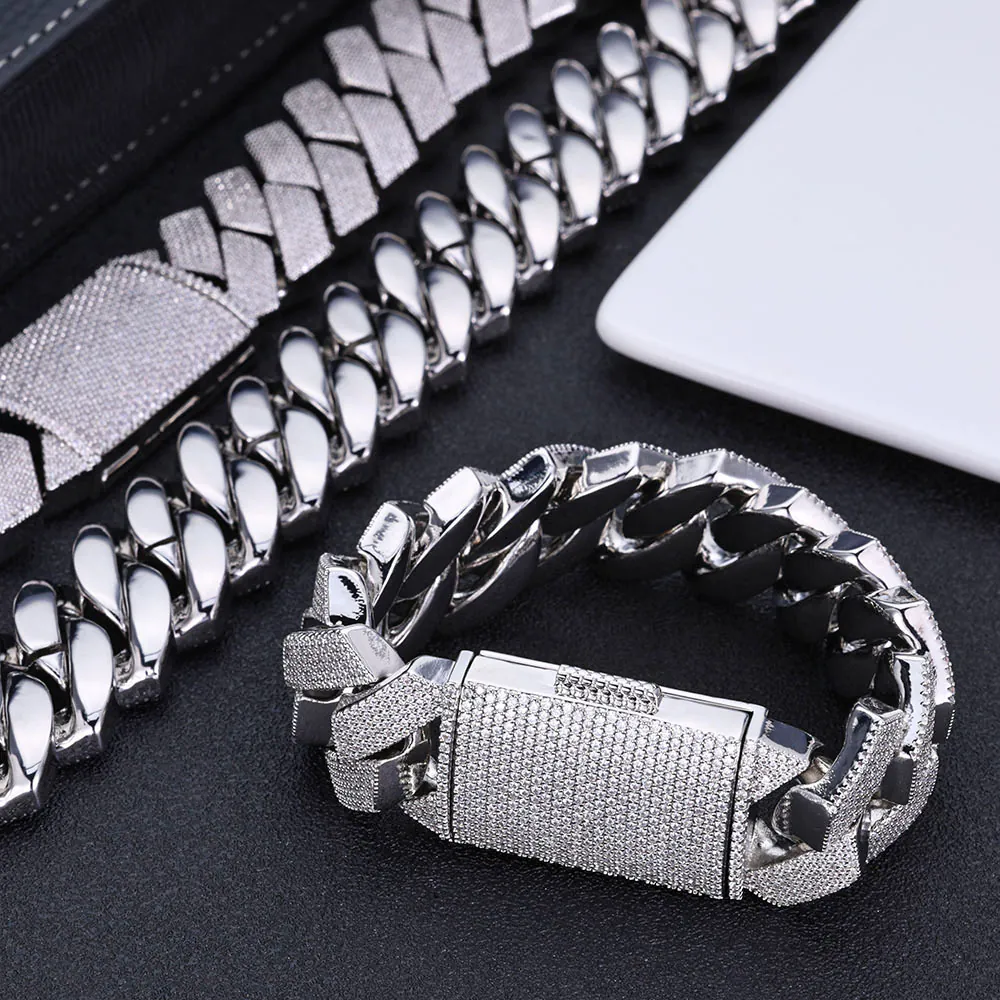 Two silver Cuban link necklaces and one bracelet on a tabletop, necklace laid flat, bracelet clasp closed and standing upright.